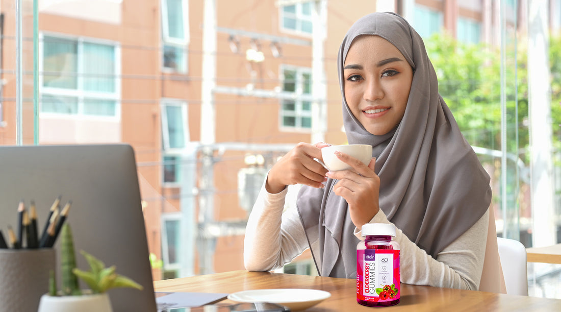 A Muslim woman wearing a hijab holds a cup of coffee while contemplating the benefits of elderberry gummies for boosting immunity