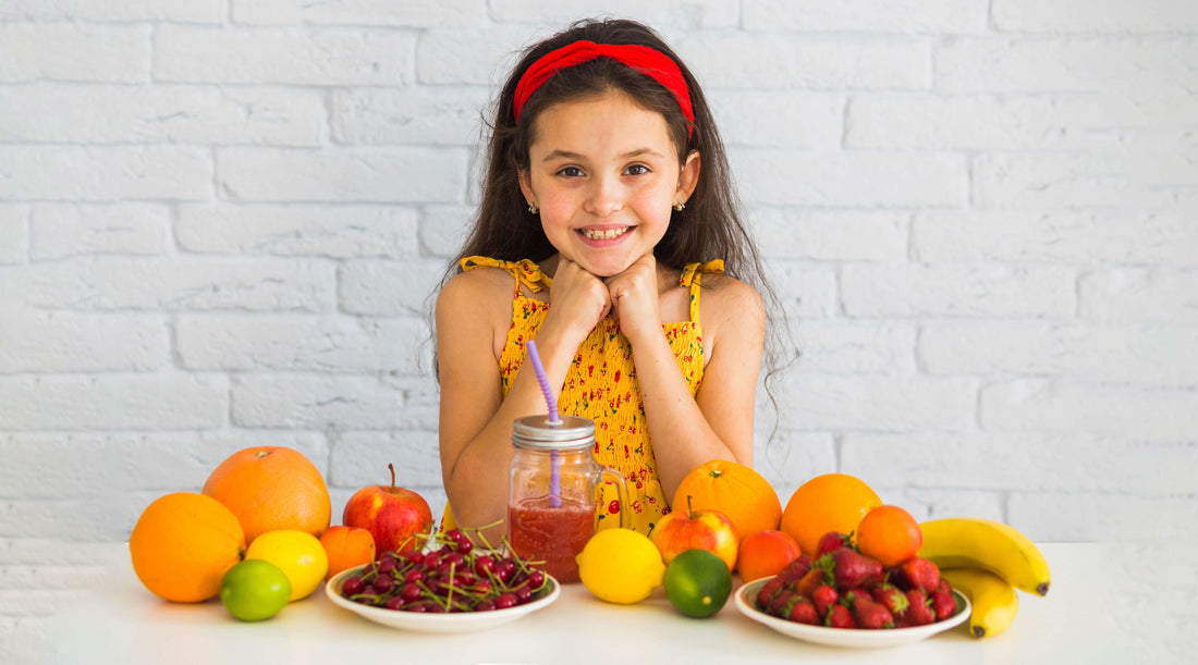 A young girl happily sits in front of a table filled with fruit and juice, promoting multivitamins for kids